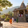 Visitors approaching a stone temple through a tree-lined courtyard